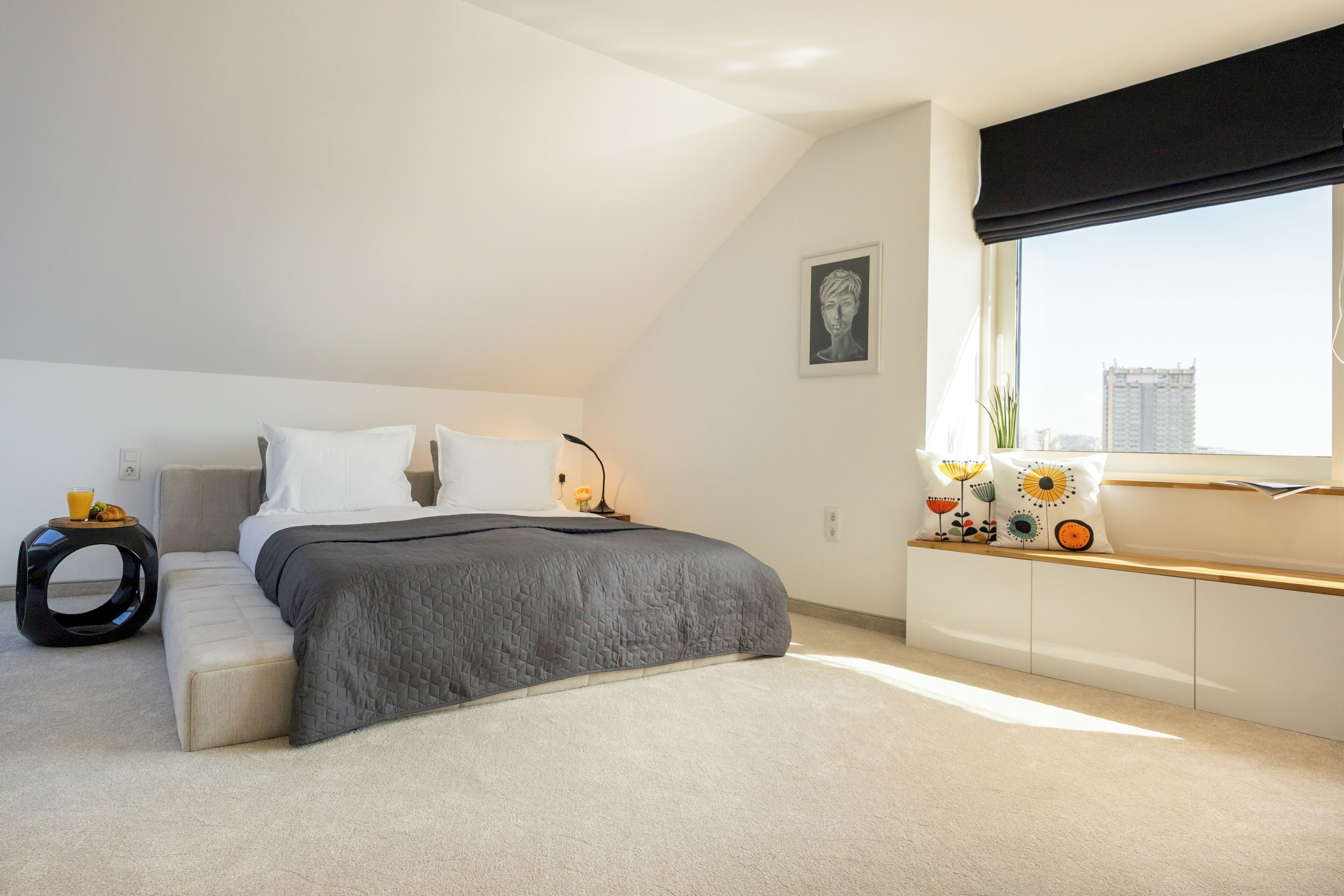 A modern bedroom with a bed, bedside table, and a window with a city view.