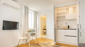 Un soggiorno moderno con una TV a schermo piatto, un'area pranzo con un piccolo tavolo e sedie, una tappeto in pelliccia e una cucina con scaffali aperti.