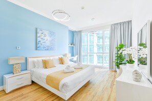 Une chambre d’hôtel moderne dotée d’un grand lit, de tables de chevet, d’un bureau et offrant une vue sur la ville grâce à de grandes fenêtres.