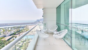 A balcony with white wicker chairs, a glass railing, and a view of a beach and resort area. - Al Bateen Ultra Luxe 5BR I Private Beach (Dubai)