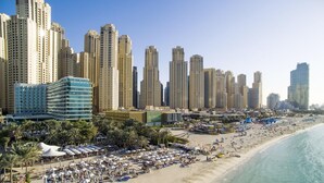 A coastal cityscape with high-rise buildings and a beach with umbrellas and sun loungers. - Al Bateen Ultra Luxe 5BR I Private Beach (Dubai)
