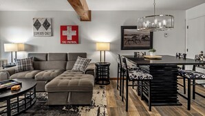 A modern living room with a sectional sofa, a dining table with benches, and a chandelier. - Timber Run — Your Perfect Steamboat Getaway, private shuttle to resort (Steamboat Springs)