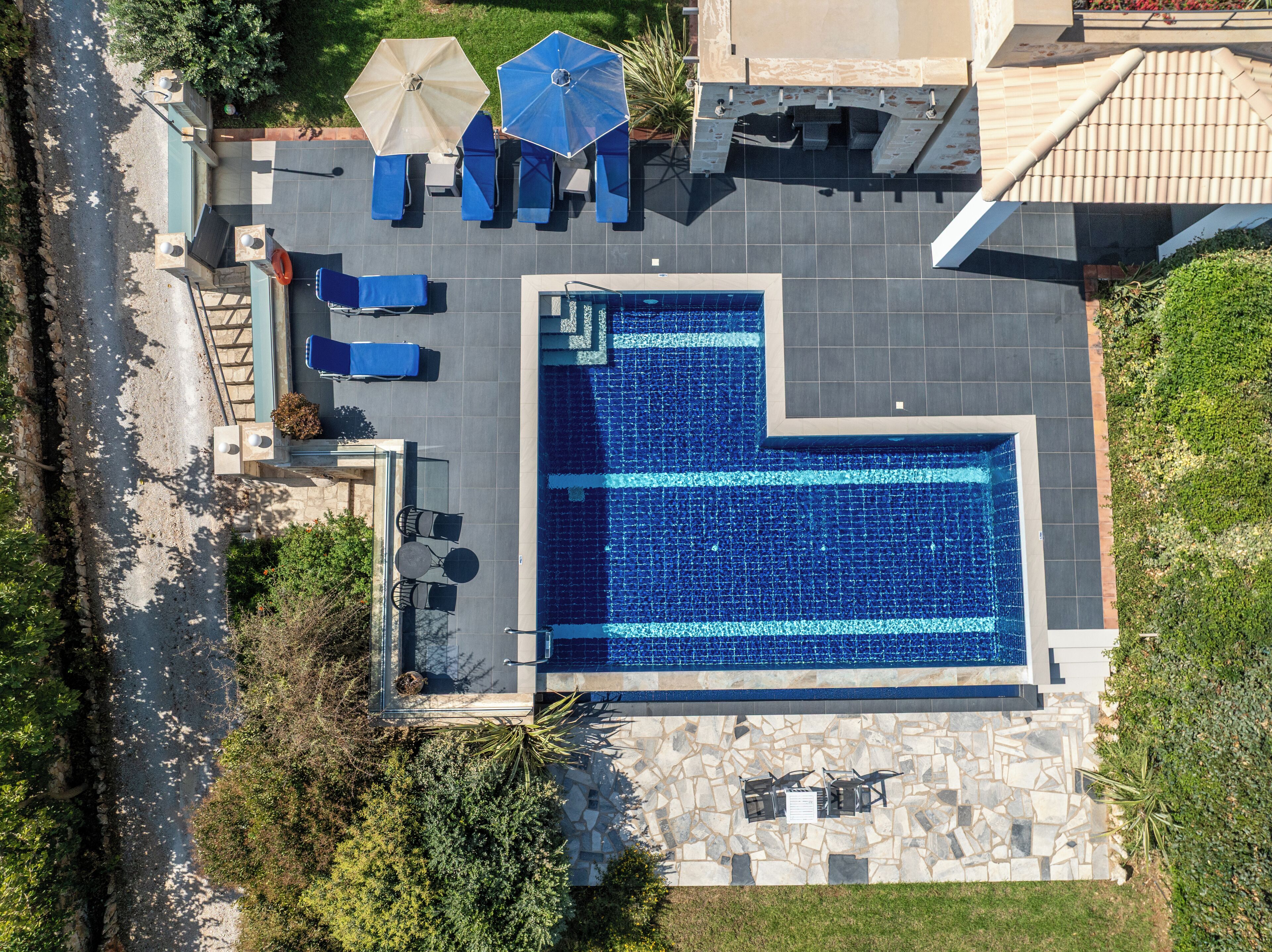A rooftop pool with a geometric design, surrounded by stone tiles and equipped with blue lounge chairs and umbrellas.