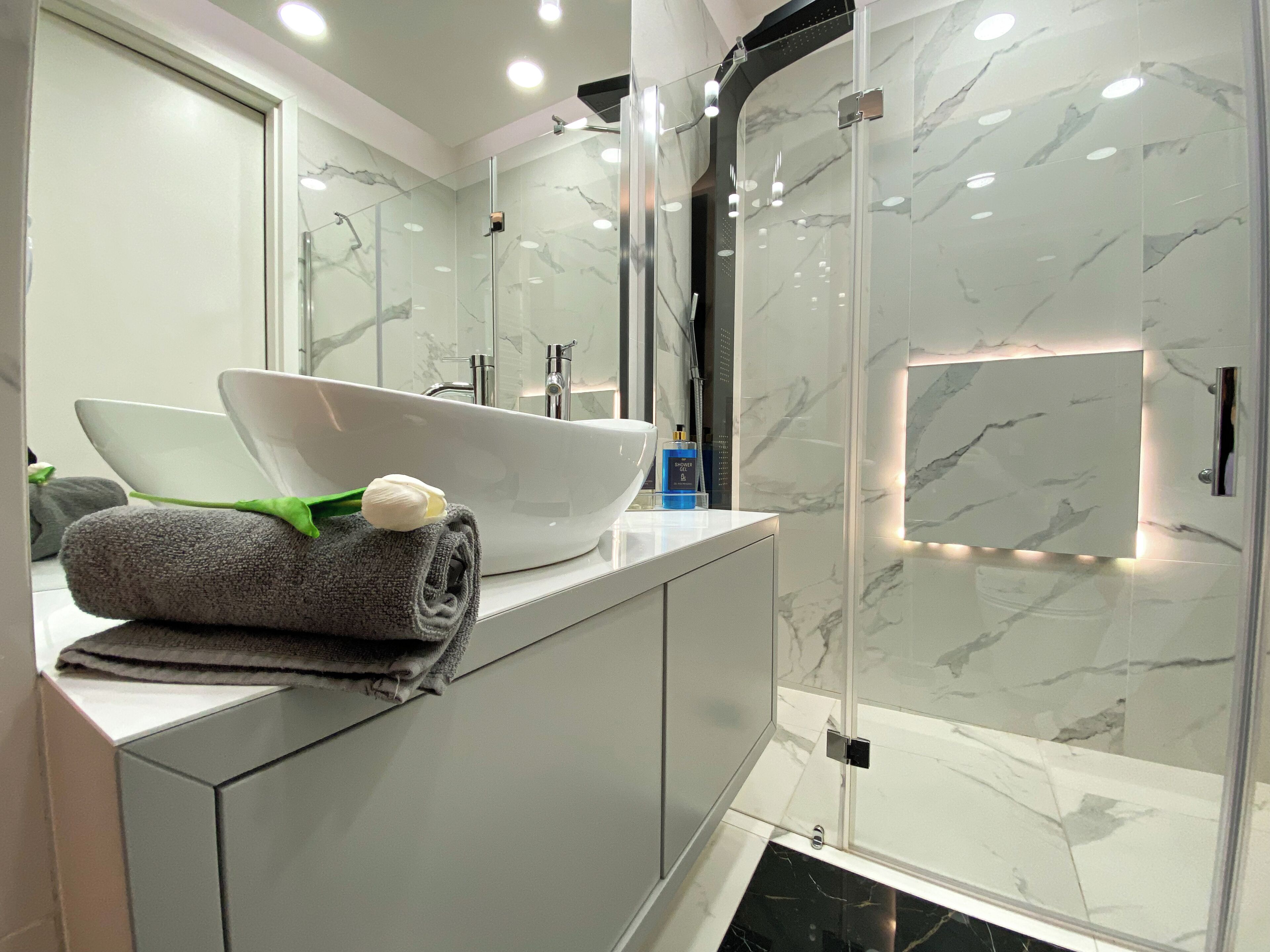A modern bathroom with a large white sink, a glass shower enclosure, and marble walls.