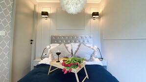 Une chambre à coucher avec un lit, des lampes de chevet, un lustre, un plateau avec des fleurs et un verre de vin.