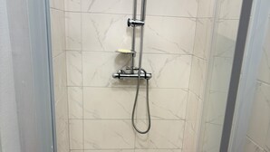 A small, enclosed shower stall with a handheld showerhead and a handheld shower attachment.