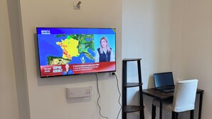 A flat-screen TV mounted on a wall displaying a news channel, a laptop on a desk, and a chair.