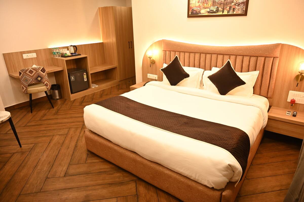 Una habitación de hotel con una cama grande, cabecera de madera, mesitas de noche, un escritorio y un armario.