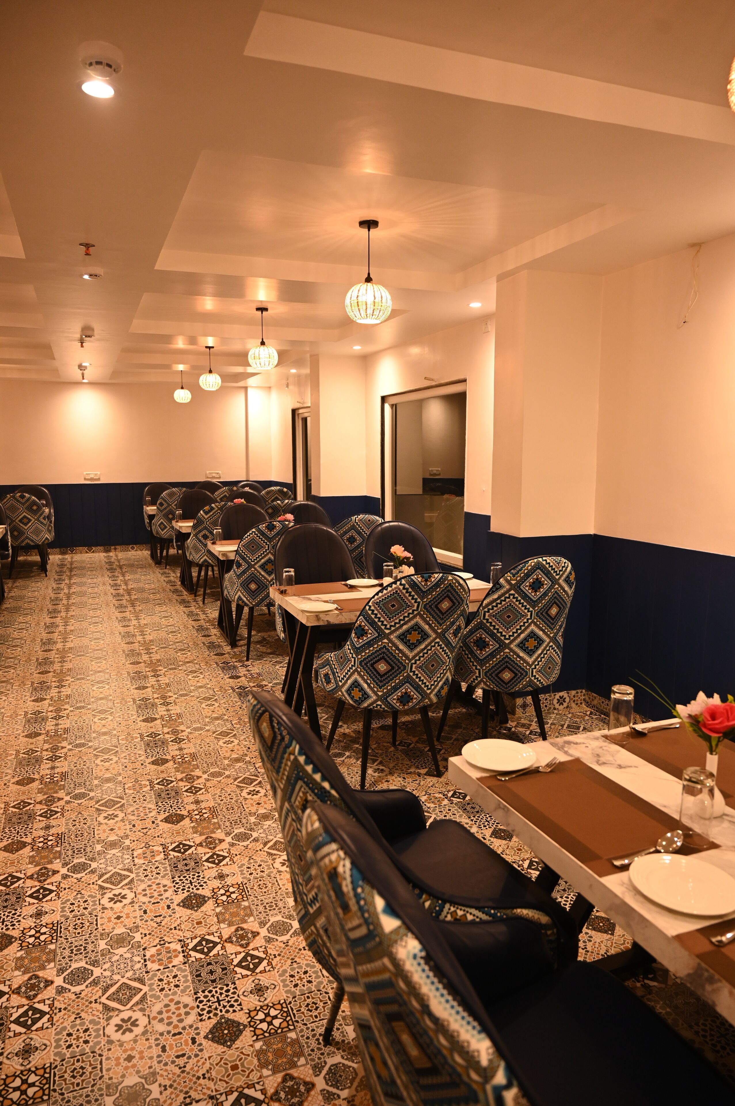 Une chambre d’hôtel avec un tapis à motifs, un coin repas avec des tables et des chaises, et un grand miroir au mur.