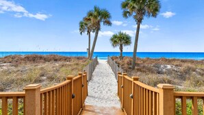 A wooden pathway leading to a beach with palm trees and a clear blue sky. - Sweeping Gulf Views! 1/2 sleeps 4! (Panama City Beach)