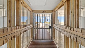 A corridor with wooden railings and a metal gate leading to a beach view. - Sweeping Gulf Views! 1/2 sleeps 4! (Panama City Beach)