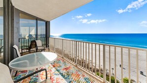 A balcony with a glass table and chairs, overlooking a beach with a clear blue sky and ocean. - Sweeping Gulf Views! 1/2 sleeps 4! (Panama City Beach)