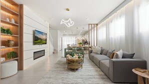 Un soggiorno moderno con un divano grigio, un tavolino e una TV fissata al muro. Si intravedono un camino, un'area pranzo e una cucina sullo sfondo.