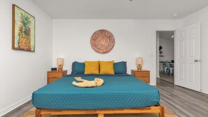Un dormitorio con una cama, dos mesitas de noche, un tapiz en la pared y una puerta que da a otra habitación.