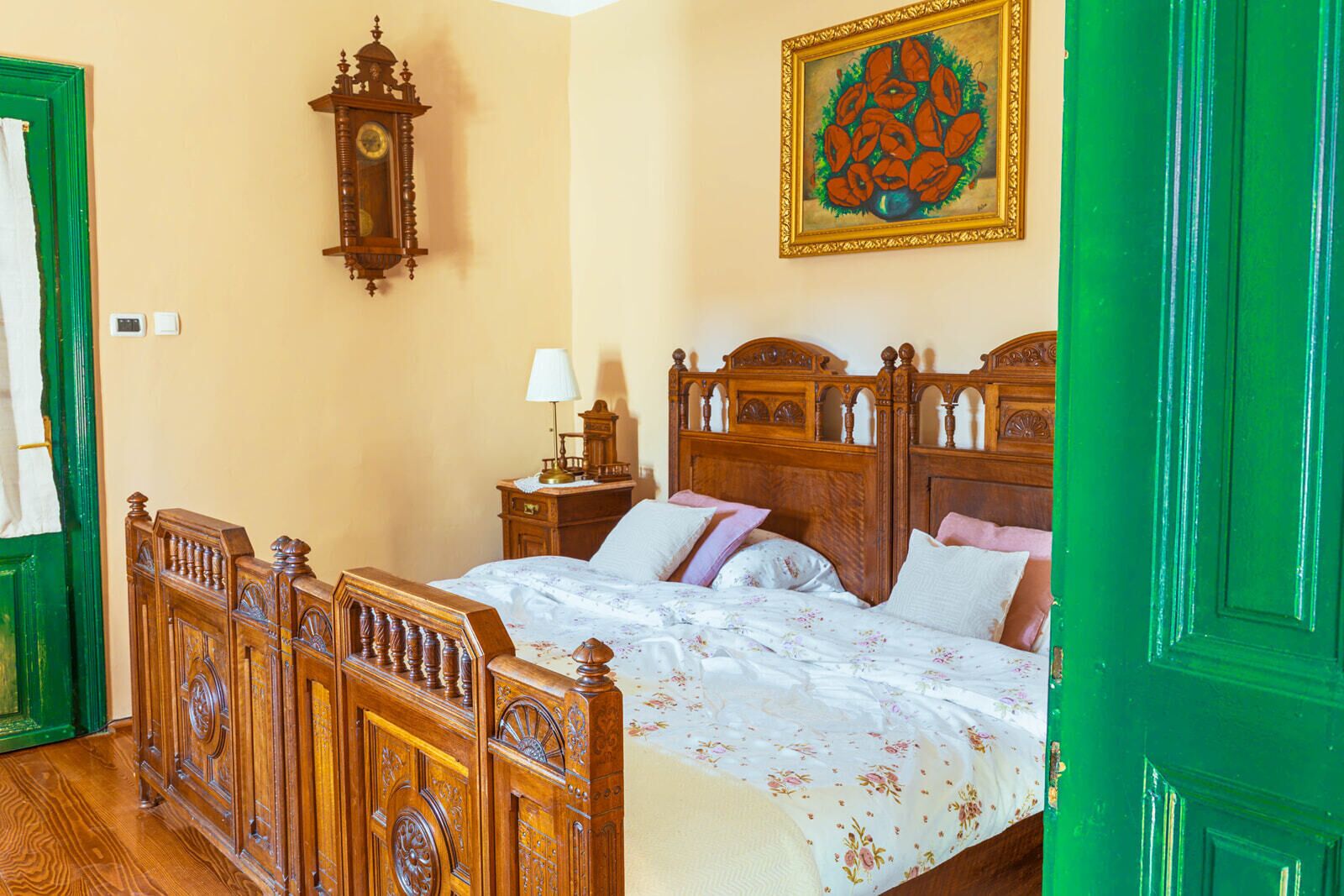 A bedroom with a wooden bed, a nightstand, a wall clock, and a painting.
