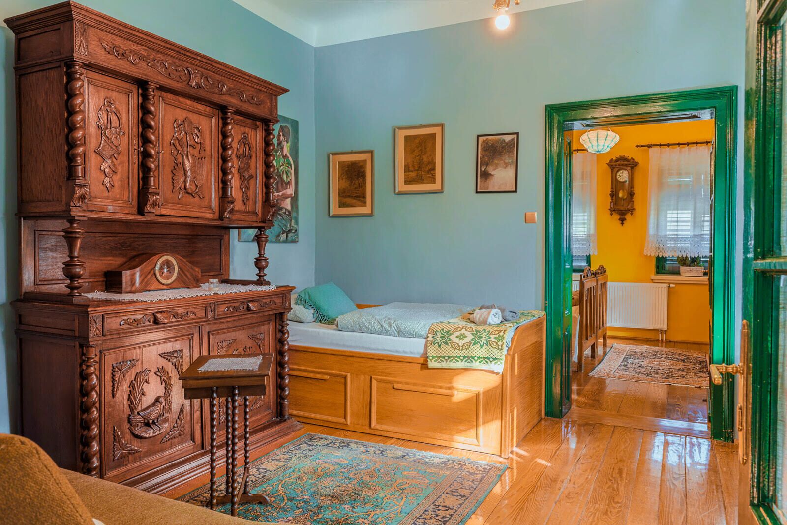 A cozy room with a wooden bed, a large wooden cabinet, and a small table. There are framed pictures on the wall and a clock on the wall.