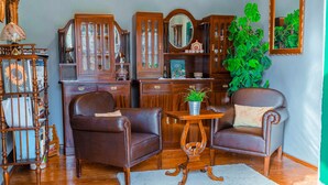 Uma sala de estar tradicional com poltronas de couro, uma mesa de centro de madeira e uma planta verde grande.