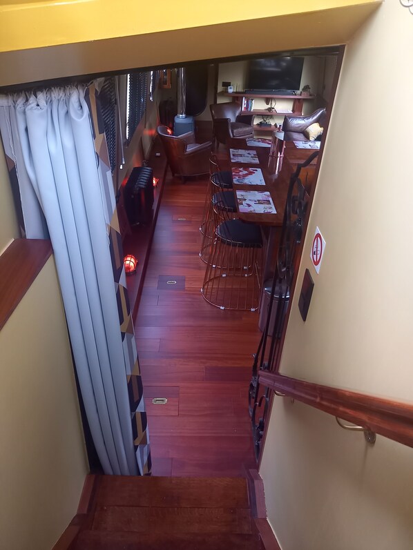 A narrow corridor leading to a dining area with a table and chairs, a television, and a staircase.