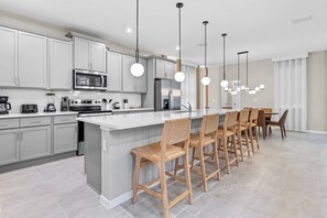 A modern kitchen with grey cabinets, a central island with bar stools, stainless steel appliances, and pendant lighting. - 6BR house with game room near Disney area (Kissimmee)