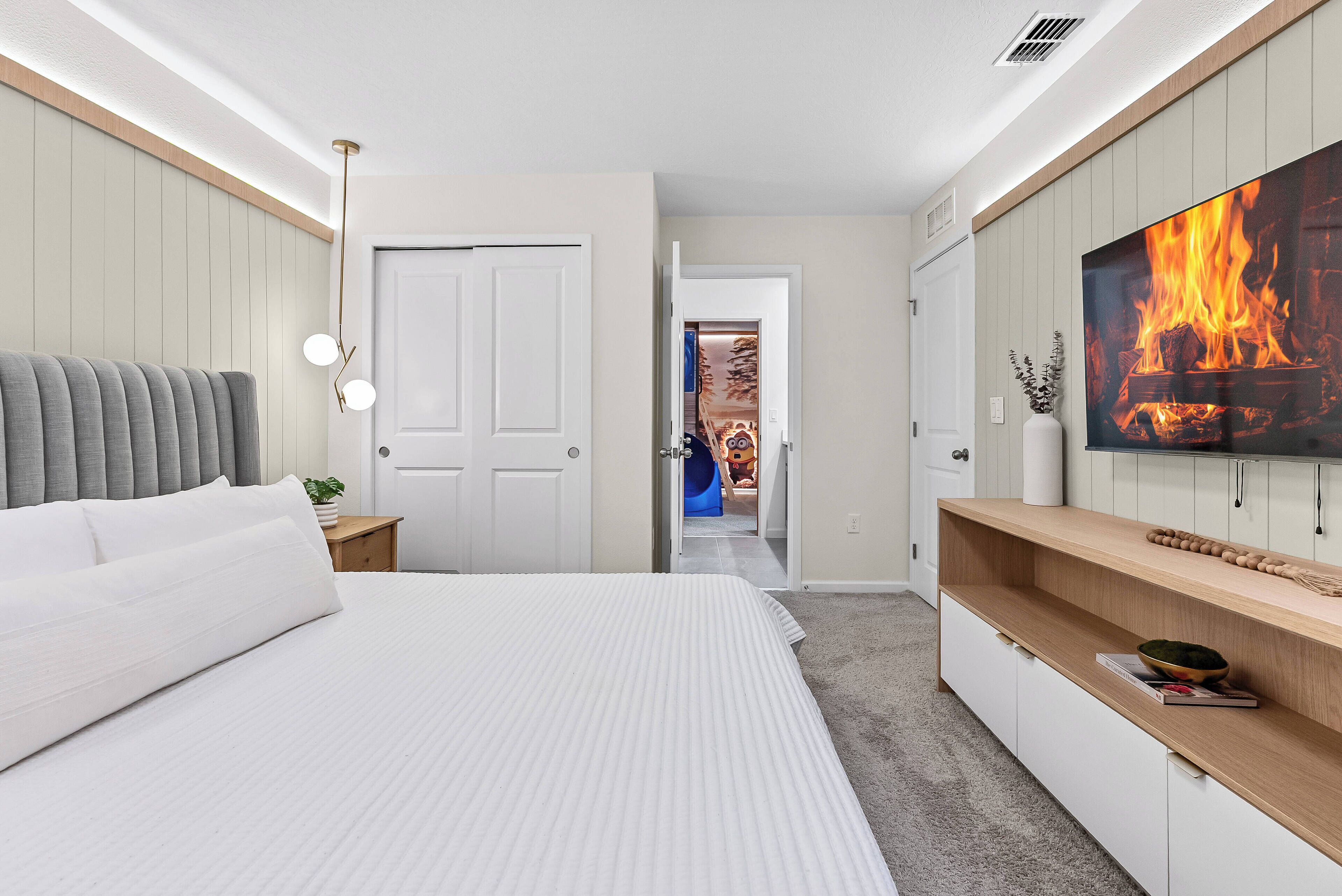 A bedroom with a bed, a TV, a fireplace, and a hallway leading to a bathroom.