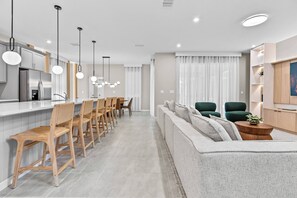 A modern kitchen with a stainless steel refrigerator, wooden chairs, and pendant lighting. - 6BR house with game room near Disney area (Kissimmee)