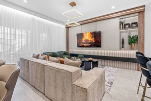 A modern living room with a sectional sofa, a flat-screen TV, and a decorative wall shelf. - 5BR house with game room near Disney area (Kissimmee)