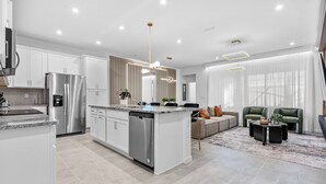 Et moderne køkken med rustfrie hårde hvidevarer, en central ø og et spiseområde med en sofa og sofabord.