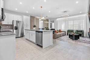 A modern kitchen with stainless steel appliances, a central island, and a dining area with a sofa and coffee table. - 5BR house with game room near Disney area (Kissimmee)
