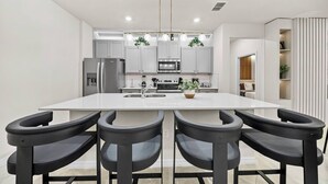 Una cucina moderna con isola centrale, quattro sgabelli neri a listello, elettrodomestici in acciaio inossidabile e luci a sospensione.