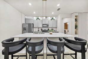 A modern kitchen with a central island, four black bar-style chairs, stainless steel appliances, and pendant lighting. - 7BR house sleeps 20 with game room (Clermont)