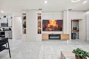 A modern living room with a large flat-screen TV, a fireplace, and built-in shelves. - 7BR house sleeps 20 with game room (Clermont)