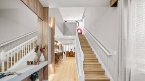 A modern interior with a wooden staircase, white railings, and a dining area with chairs and tables. - 7BR house sleeps 20 with pool table (Clermont)