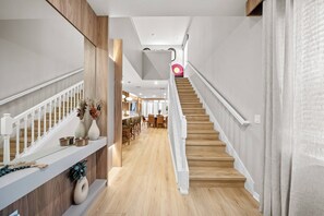 A modern interior with a wooden staircase, white railings, and a dining area with chairs and tables. - 7BR house sleeps 20 with pool table (Clermont)
