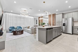 A modern kitchen with stainless steel appliances, a central island, and a dining area with a sofa and coffee table. - 5BR house sleeps 14 with private pool in kissimmee (Kissimmee)