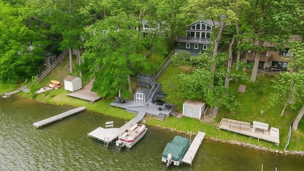 Een vakantiehuis aan een meer, met een aanlegsteiger, een boot en een huis omringd door bomen.