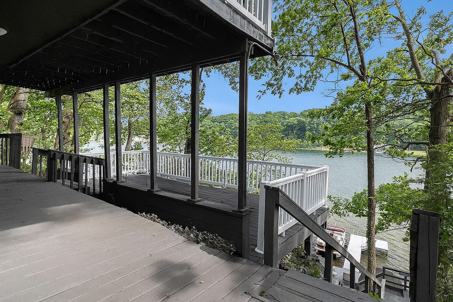 A wooden deck with a railing overlooking a lake, surrounded by trees.
