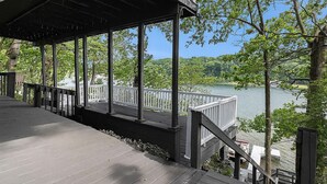 Een houten terras met een balustrade dat uitkijkt over een meer, omringd door bomen.