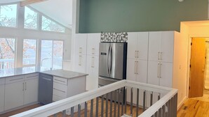 Een moderne keuken met witte kasten, een roestvrijstalen koelkast en een groot raam met uitzicht op een balkon.