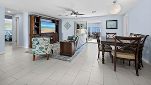 A spacious living room with a large flat-screen TV, a dining area with a wooden table and chairs, and a ceiling fan. - Longboat Key - Choose Joy - Relax on the Beach (Longboat Key)