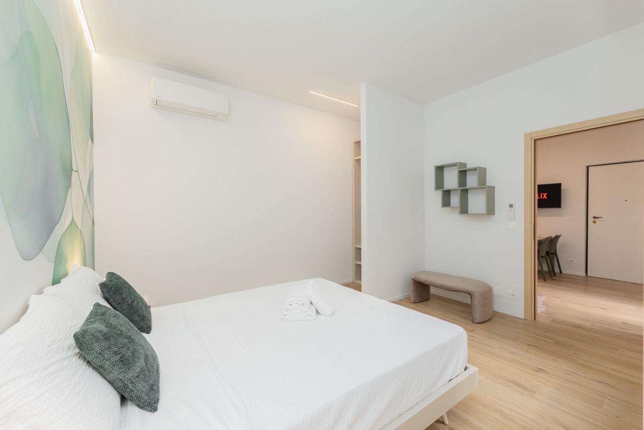 Une chambre d’hôtel moderne avec un lit bien fait, un banc et un téléviseur fixé au mur.