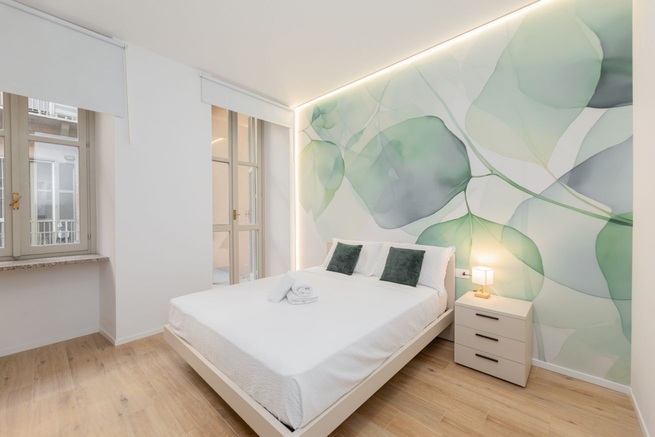 Un dormitorio moderno con cama, mesita de noche y pared con diseño de hojas.