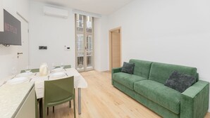 A modern living room with a green sofa, a dining table set for two, and a flat-screen TV mounted on the wall. - Torino | San Domenico Home (Torino)