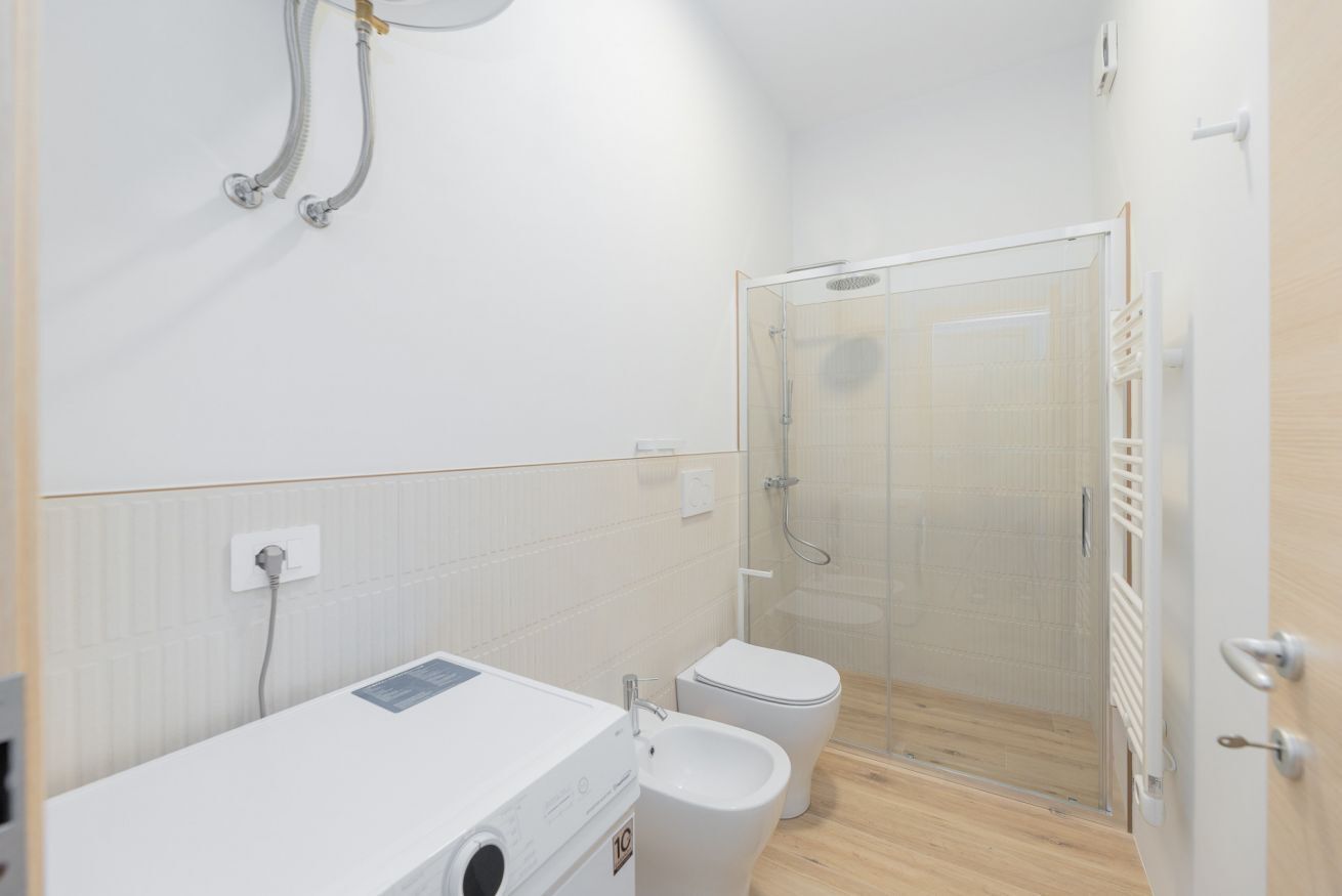 Une petite salle de bain comprenant un espace douche, des toilettes et un lave-linge.