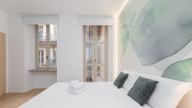A modern hotel room with a large bed, a view of the city through a window, and a minimalist design. - Torino | San Domenico Home (Torino)