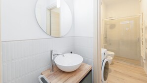 A modern bathroom with a round mirror, a white sink, and a glass-enclosed shower. - Torino | San Domenico Home (Torino)