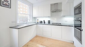 A modern kitchen with white cabinets, a large window, and built-in appliances. - Hyde Park 3BR Retreat by Marble Arch (London)