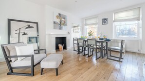 A modern living room with a fireplace, a dining area with a table and chairs, and a large window with a view of the outside. - Hyde Park 3BR Retreat by Marble Arch (London)
