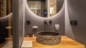 Une salle de bain moderne avec un miroir rond, un lavabo en pierre et des serviettes soigneusement pliées sur une étagère en bois.