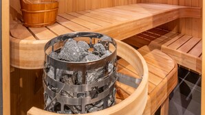 Un sauna en bois, avec des bancs, un seau et un récipient en métal pour les pierres.