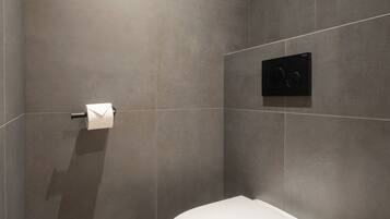 Een moderne badkamer met een wit toilet, een zwarte prullenbak en een papieren handdoekdispenser aan de muur.